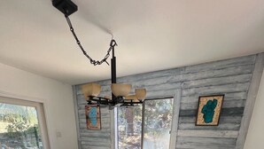 Un comedor con mesa y sillas de madera, una araña y vistas a través de un ventanal corredero.