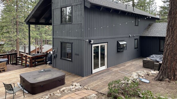 Una cabaña moderna de dos pisos con terraza, mobiliario exterior y un jacuzzi.