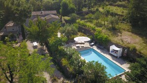 A pool surrounded by lush greenery, a stone house, and a gazebo.