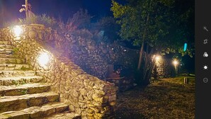 A stone staircase leading up to a stone wall, surrounded by trees and illuminated by lights.