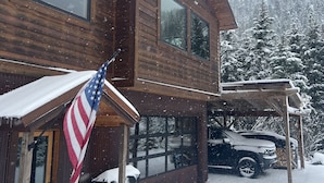 Uma cabana de madeira com janelas amplas, uma bandeira americana e uma paisagem coberta de neve.