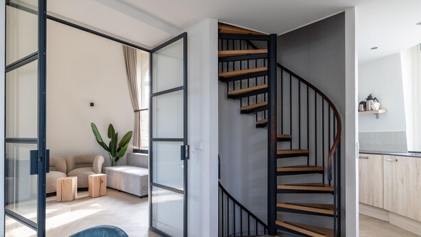 Ein modernes Interieur mit einer Wendeltreppe, einer Sitzecke mit Pflanze und einem Küchenbereich.