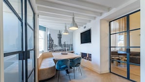 Ein modernes Interieur mit einem Holzesstisch, blauen Stühlen, einer eingebauten Bank, einem Kamin und einem großen Fenster mit Blick auf die Stadt.