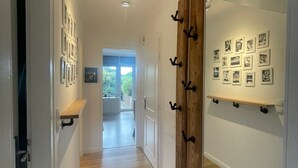 A hallway with wooden flooring, a wooden door with black hooks, and a wall with framed pictures. - PiPPA - PIPPA, Germany (List)