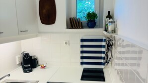 A kitchen with white cabinets, a built-in oven, a sink, and a window with a view of greenery. - PiPPA - PIPPA, Germany (List)