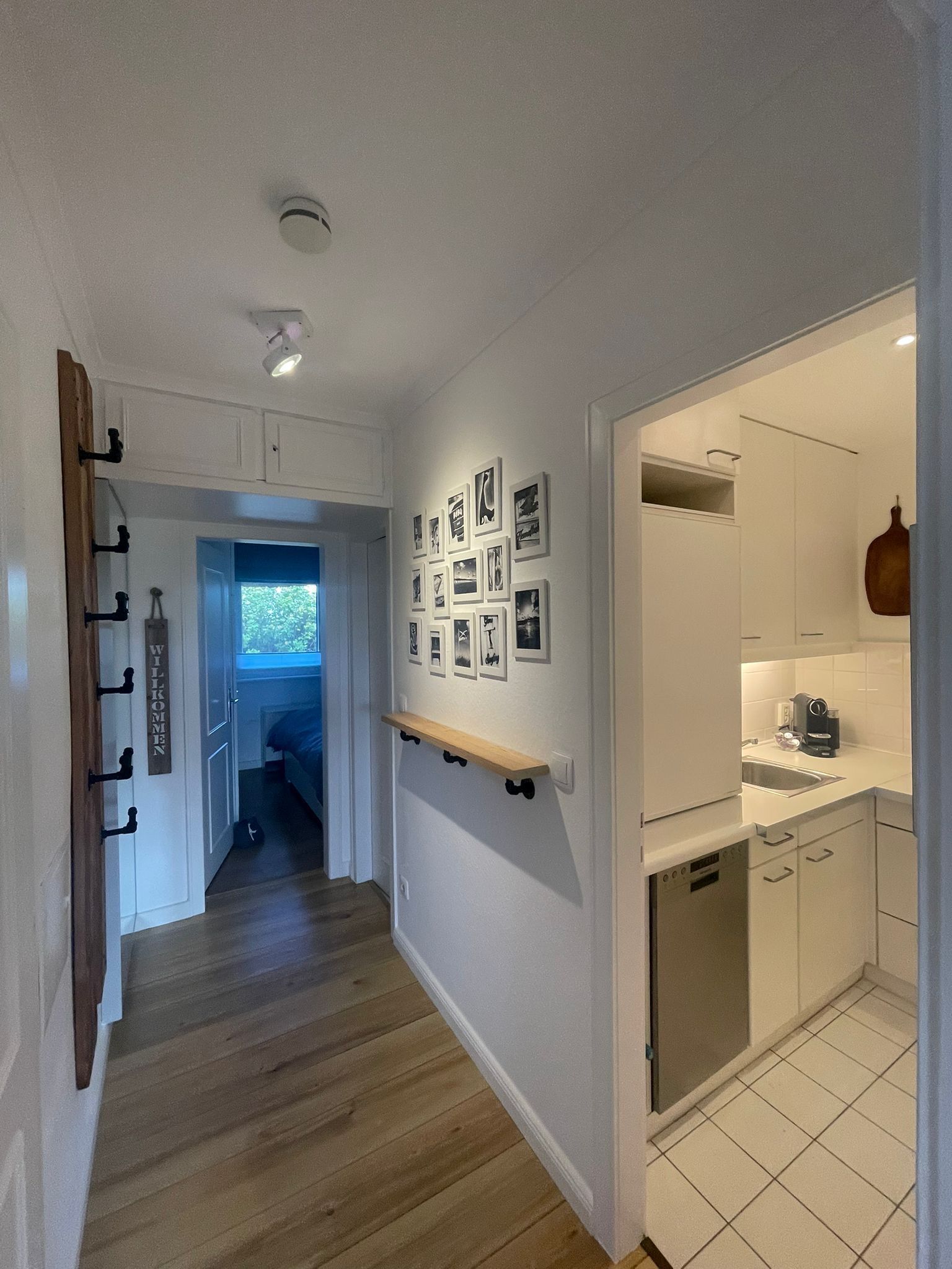 Ein Flur mit Holzboden, einer an der Wand befestigten Ablage und einer Reihe gerahmter Bilder.