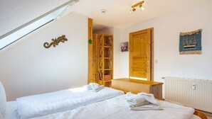 Een slaapkamer met twee bedden, een houten garderobe, een houten plank en een klein raam.