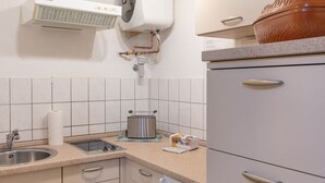 Een keuken met witte kastjes, een roestvrijstalen spoelbak, een waterkoker en een brooddoos.