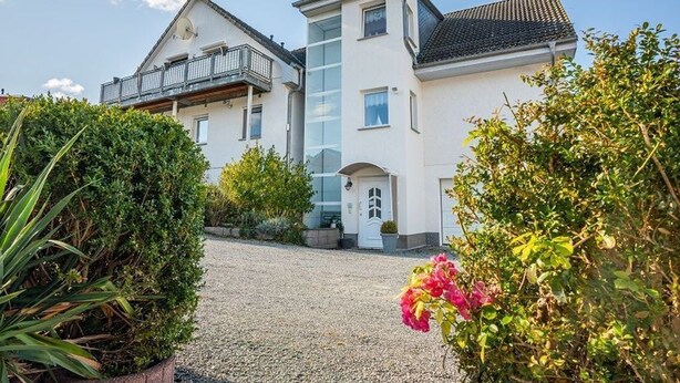 A two-story house with a balcony, a gravel driveway, and surrounding greenery. - Apartment Pier 4 - Holiday apartments Hagen (Zinnowitz)
