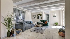 Amplio salón con un sofá gris, una mesa de centro y un sofá verde. Hay plantas y una cesta en el suelo.