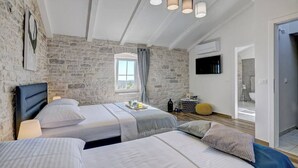 Un dormitorio con dos camas, una pared de piedra, una ventana y un televisor instalado en la pared.