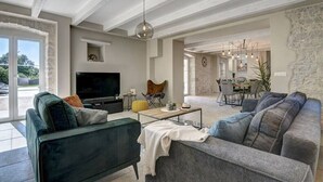 Amplia sala de estar con televisor grande, asientos cómodos y un comedor al fondo.