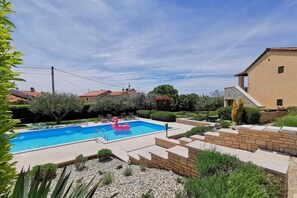 A swimming pool with a pink flamingo float, surrounded by a landscaped garden with various plants and a stone wall.