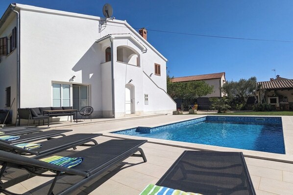 Une villa blanche avec une piscine, un espace salon extérieur et un ciel d’un bleu limpide.