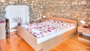 A bedroom with a stone wall, wooden floor, a bed with floral bedding, a nightstand, and a bedside table with a lamp. - Istrian stone house with pool for 8 persons (Gajana)