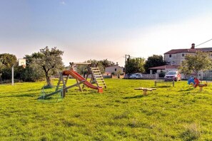 Un parque infantil con tobogán y estructura para escalar en una zona verde, con casas al fondo.