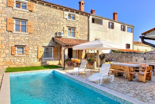 Un edificio de piedra con piscina, mobiliario de exterior y un patio cubierto.