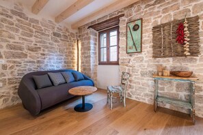 A rustic room with a stone wall, a wooden ceiling, a sofa, a chair, a small table, and a window with a view.