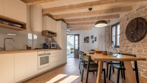 A modern kitchen with white cabinets, a wooden dining table, and a stone wall. - 5 star holiday home in the old town of Bale (Bale)