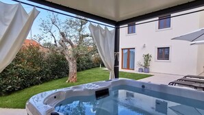 A hot tub in a covered outdoor area with a view of a white building and a tree. - Gorgeous vacation home with jacuzzi in Bale (Bale)