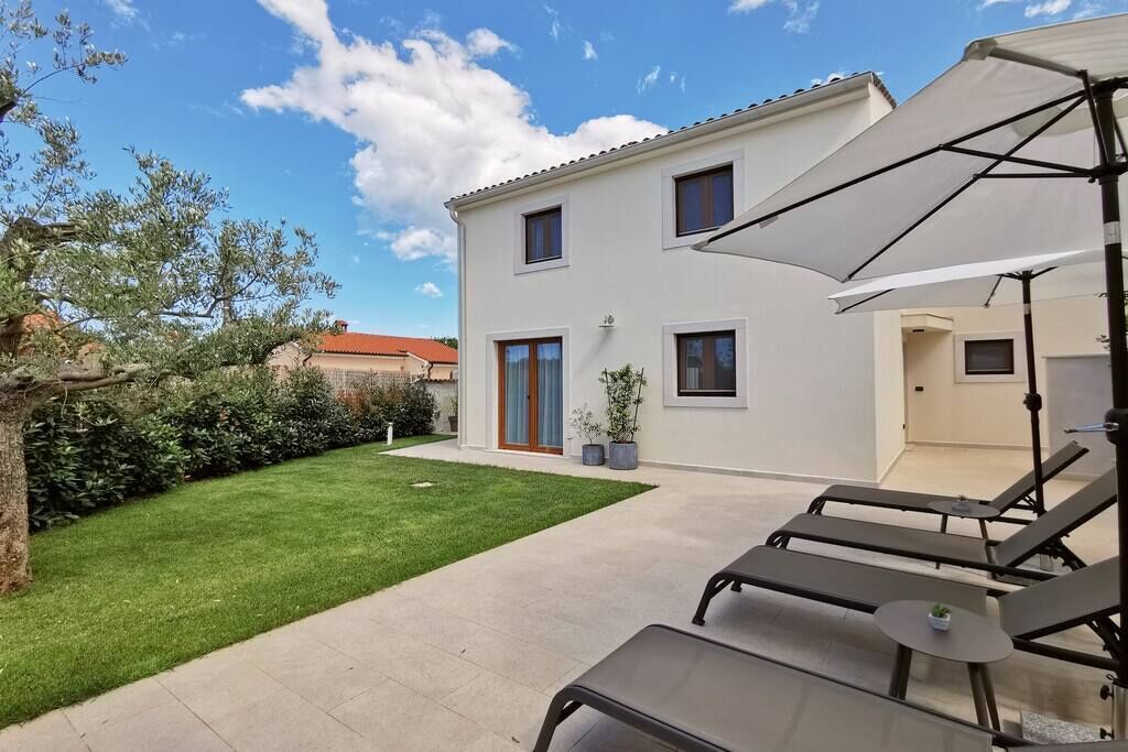 A two-story house with a well-maintained lawn, a patio with lounge chairs, and a large umbrella.