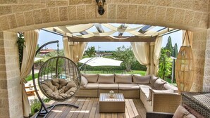Un patio exterior con un sofá acolchado, una silla colgante y una mesa.