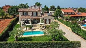 Una casa de dos pisos con piscina, rodeada de jardines cuidados y viviendas vecinas.