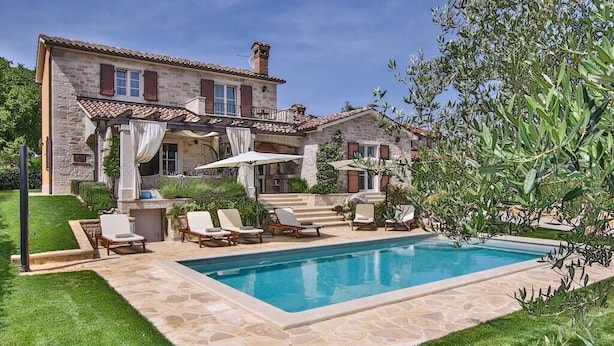 Una casa de piedra con piscina, zona de estar exterior y una pérgola.