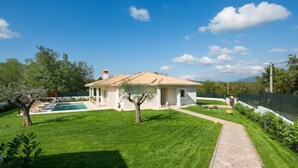Una casa con techo de tejas, piscina y césped cuidado.