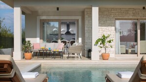 Un área junto a la piscina con sillas de descanso, una mesa con sillas y una planta en maceta.