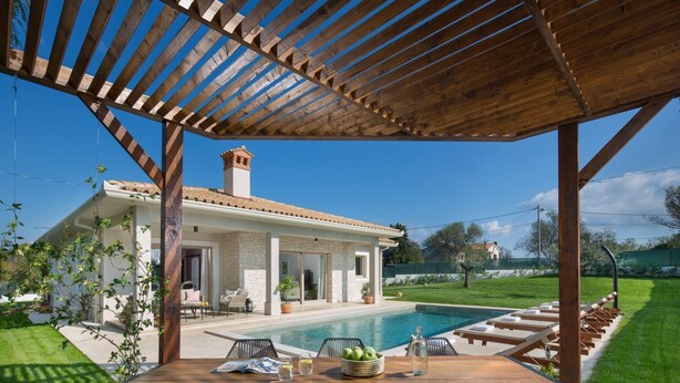 Un espacio exterior techado con piscina, sillones de descanso y una mesa con fruta y bebidas.
