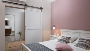 Un dormitorio con cama, mesita de noche, lámpara y una puerta corredera que da al baño.