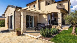 Una casa de dos pisos con un patio que cuenta con mobiliario exterior y un hogar para fogata.