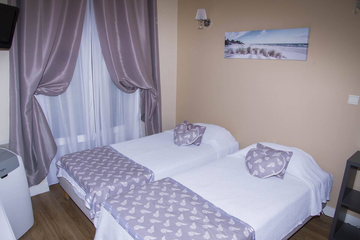 A bedroom with two beds, a bedside table, a lamp, and a painting on the wall.