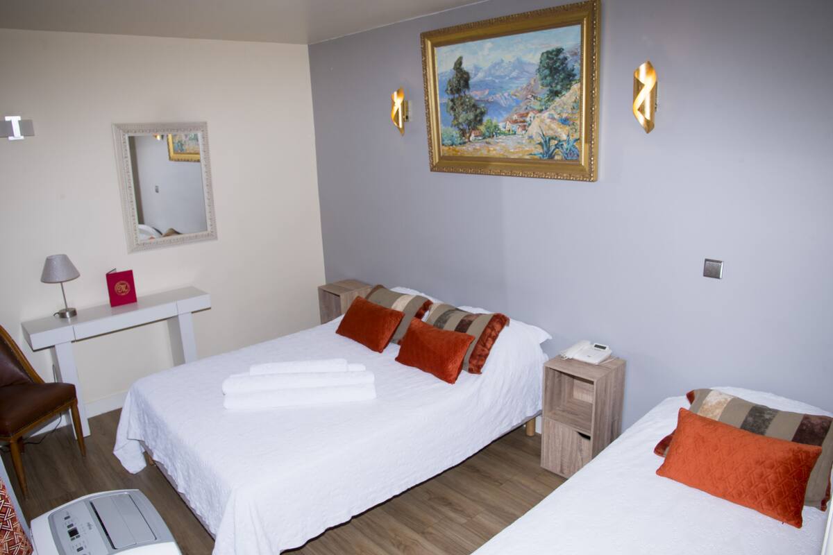 A hotel room with a bed, a desk, a chair, a mirror, and a painting on the wall.