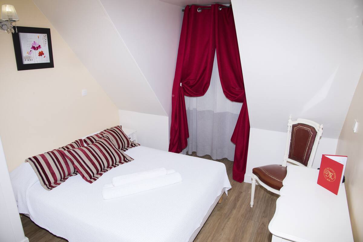 A bedroom with a bed, a chair, a red curtain, and a framed picture on the wall.