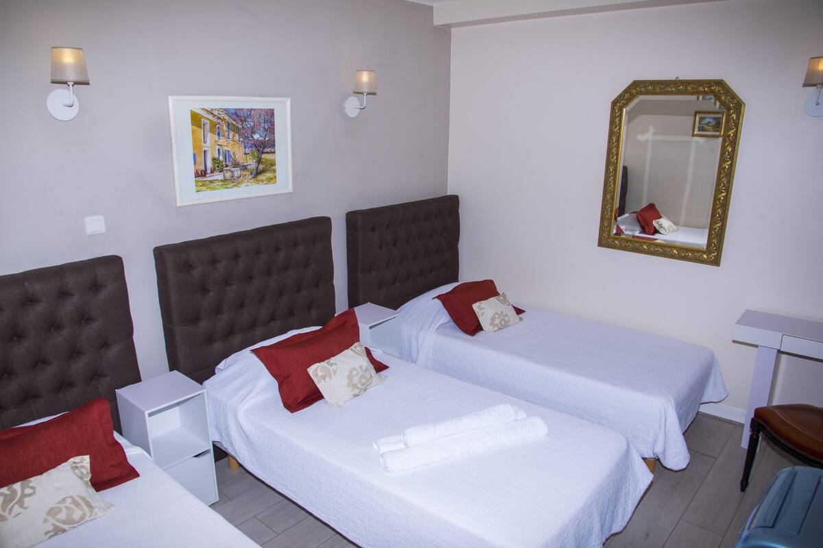 A hotel room with two beds, each with a red and beige pillow, a white nightstand, a white desk, and a mirror with a gold frame.
