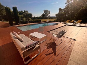 A poolside area with lounge chairs, a table, and a wooden deck. - In the heart of the Drôme Provençale (Châteauneuf-du-Rhône)