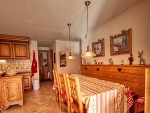 Eine Küche mit Holzausstattung, einem Esstisch mit Stühlen, einer Hängeleuchte und einer Wand mit gerahmten Bildern.