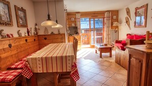 A cozy, rustic dining area with a wooden bench, a table with a striped tablecloth, and a view of a balcony with wooden railings. - Lovely 3-bed apartment, mountain decor, ski-in/ski-out (Morillon 1100)