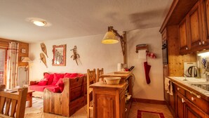 A cozy living room with a red sofa, wooden dining table, and kitchen area with wooden cabinets and a tiled floor. - Lovely 3-bed apartment, mountain decor, ski-in/ski-out (Morillon 1100)