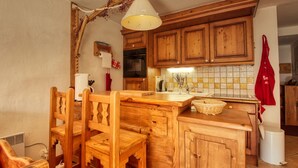 A rustic kitchen with wooden cabinets, a wooden dining table, and chairs. There is a hanging light fixture above the counter. - Lovely 3-bed apartment, mountain decor, ski-in/ski-out (Morillon 1100)