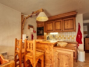 Une cuisine rustique avec des meubles de rangement en bois, une table à manger en bois et des chaises. Un luminaire suspendu se trouve au-dessus du comptoir.