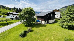 A modern two-story house with a large tree in the front yard, a paved driveway, and a mountain backdrop. - Studio with alcove, sleeps 4 in Demi-Quartier, includes parking (Demi-Quartier)