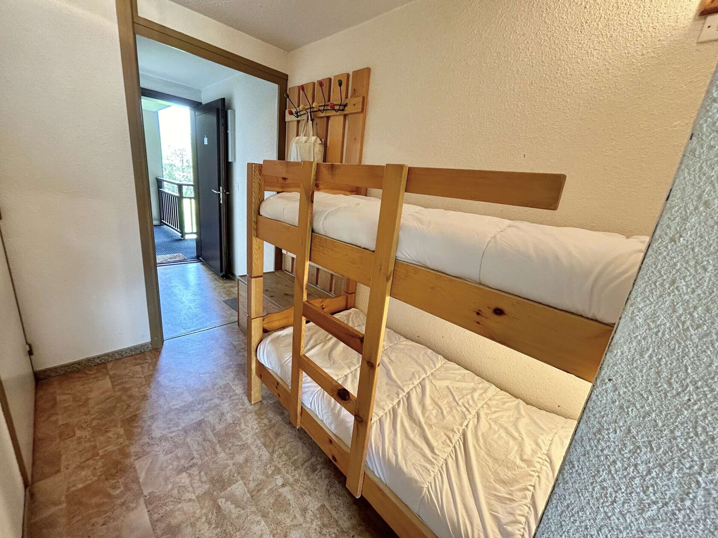 Een stapelbed met wit beddengoed in een kamer met een betegelde vloer en een houten deur.