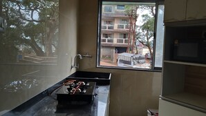 Een kleine keuken met een gasfornuis, een spoelbak en een raam met uitzicht op een woonwijk.