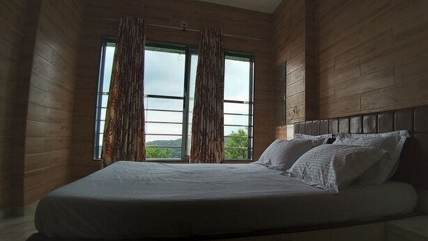 Een slaapkamer met een groot bed, houten wanden en uitzicht op groen.