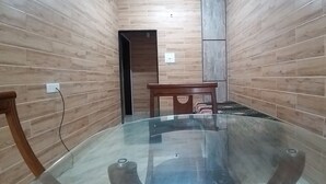 Een kamer met een glazen tafel, houten wanden, een houten stoel en een klein tafeltje.