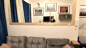 A grey sofa with tufted cushions and two pink pillows, a large mirror above it, and a wall with framed pictures and a telephone. - Citizen Arts Apartment in a heart of Radom (Radom)