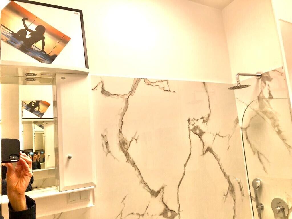 A bathroom with a marble wall, a shower, and a mirror.